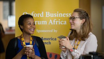 Two women talking and standing in front of a Oxford Business Forum Africa banner