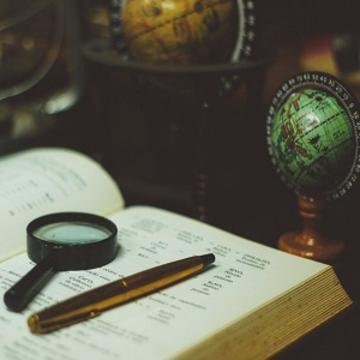 An open book sat next to a mini globe with a magnifying glass and pen