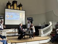 Speakers sat in front of an audience talking at an event