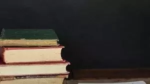 A pile of books sat next to a pad of paper and a pen