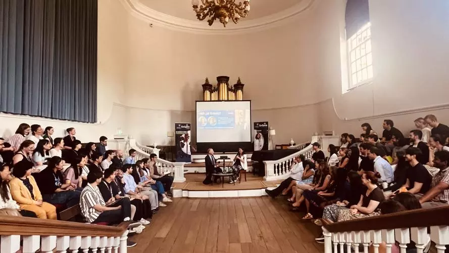two speakers sat in front of a audience giving a talk
