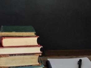 A pile of books sat next to a pad of paper and a pen